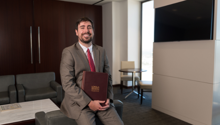 Student smiles while holding a padfolio from Loyola University New Orleans College of Law.