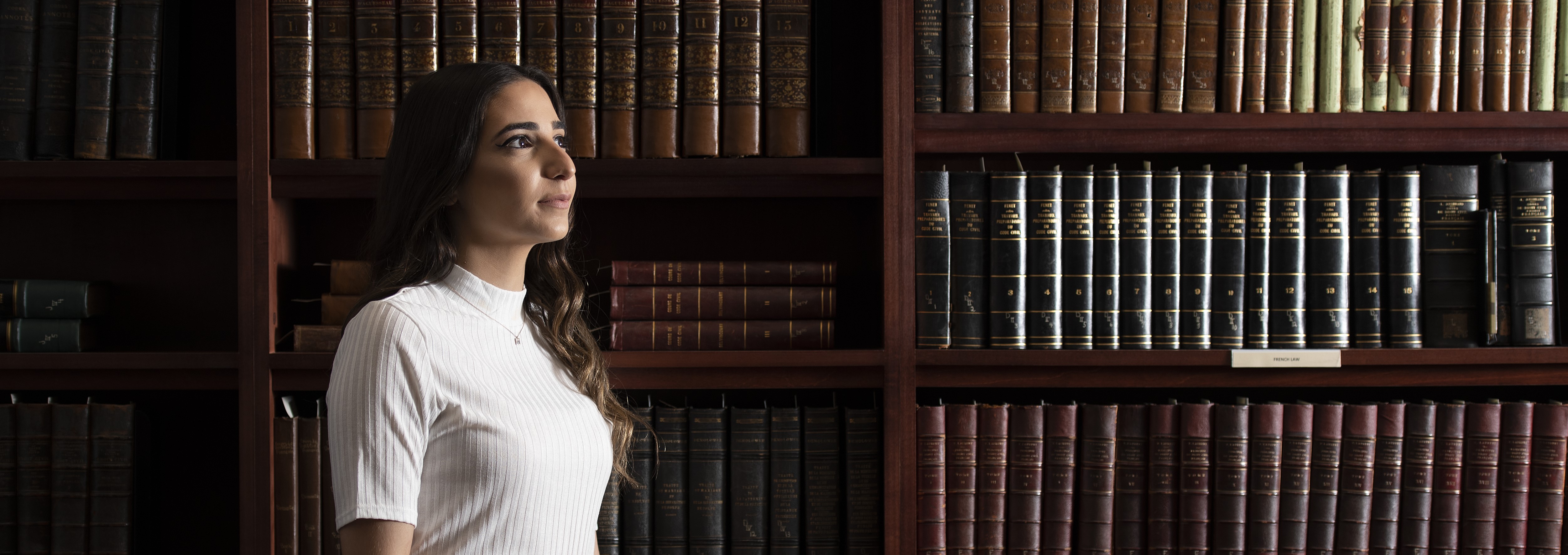 Woman stands in front of books in left facing profile
