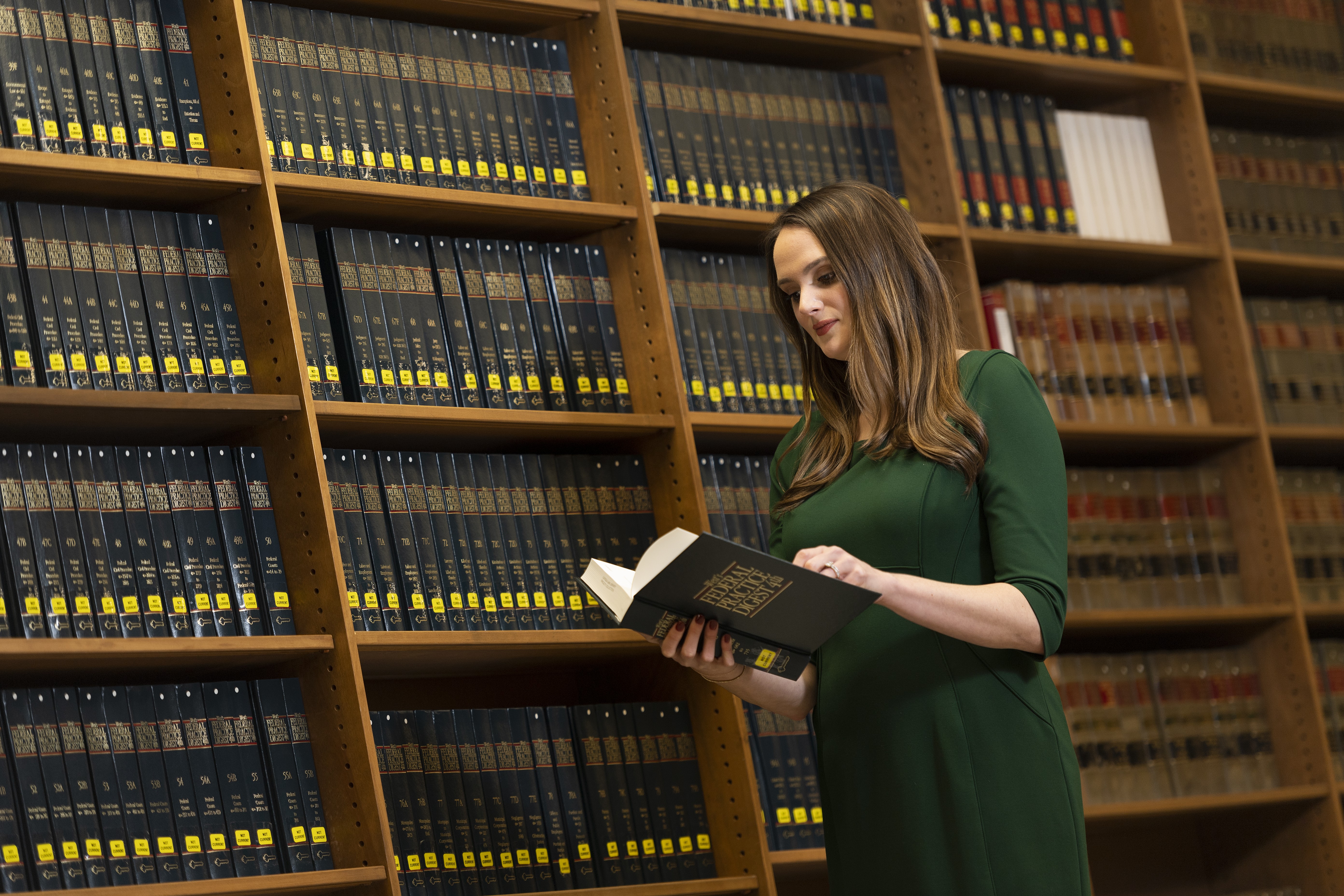 A student reads a book while standing in front of a bookshelf.