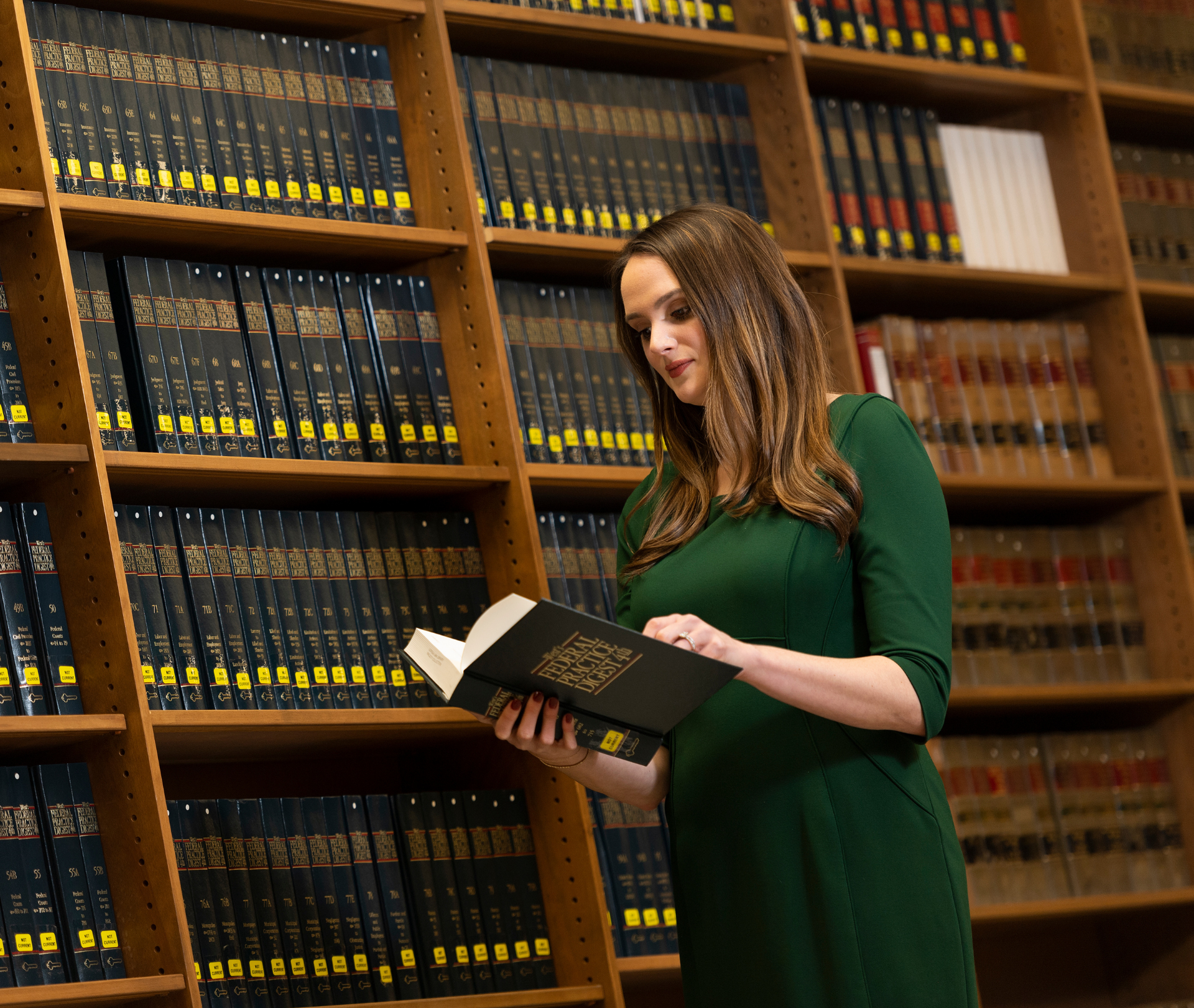 A student reads a book while standing in front of a bookshelf.