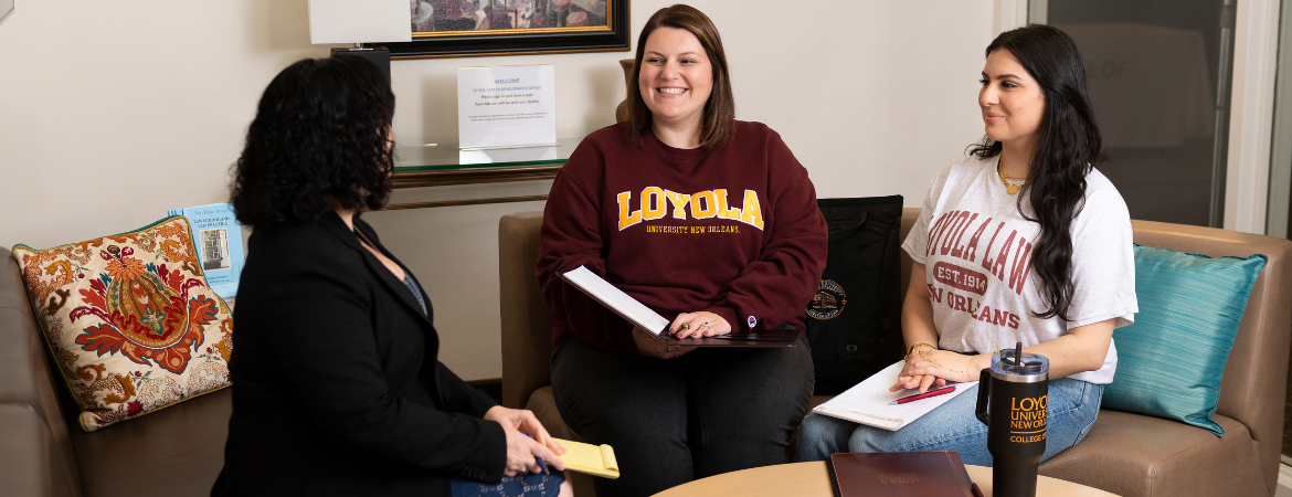 Two students in Loyola University New Orleans shirts sit with a career advisor.