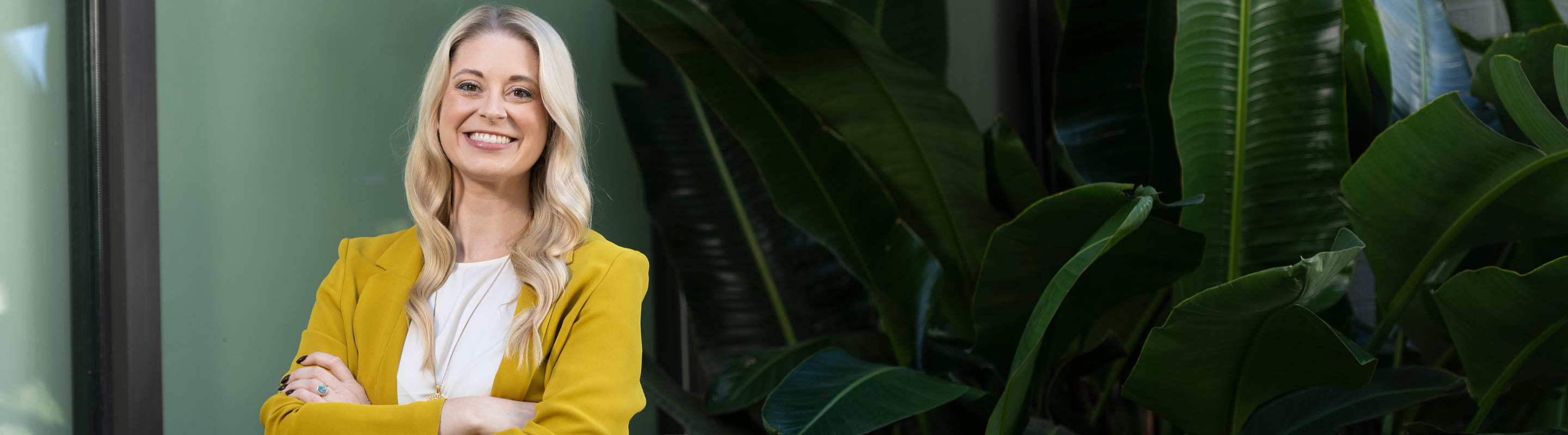 Woman in yellow blazer smiling with arms crossed.