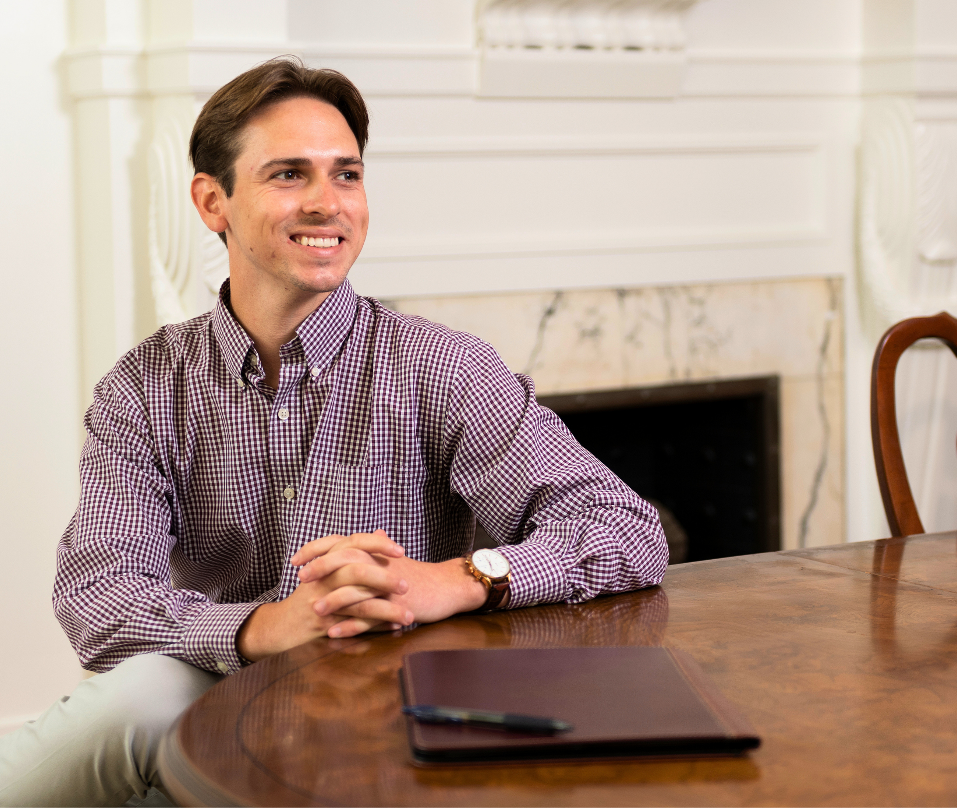 Man in maroon gingham shirt sitting at a table.